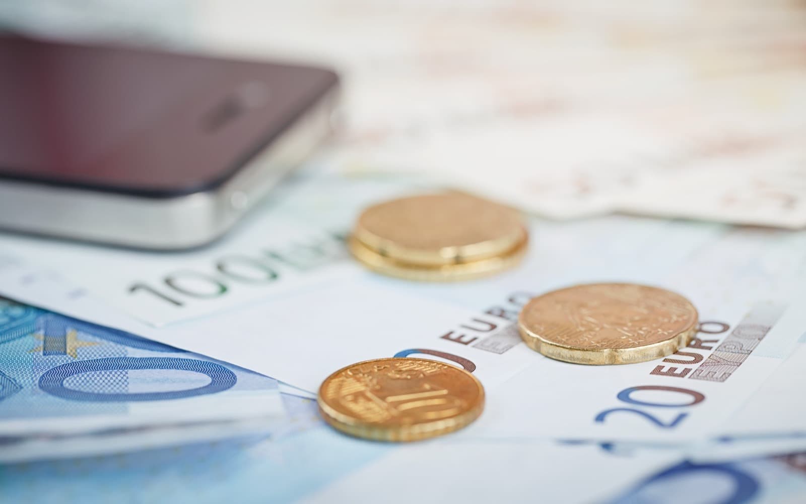 Euro banknotes and coins on a table beside a smartphone