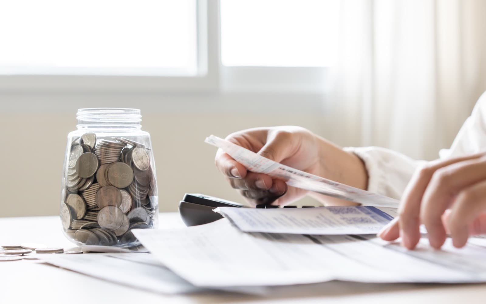Person reviewing household bills beside a jar of coins