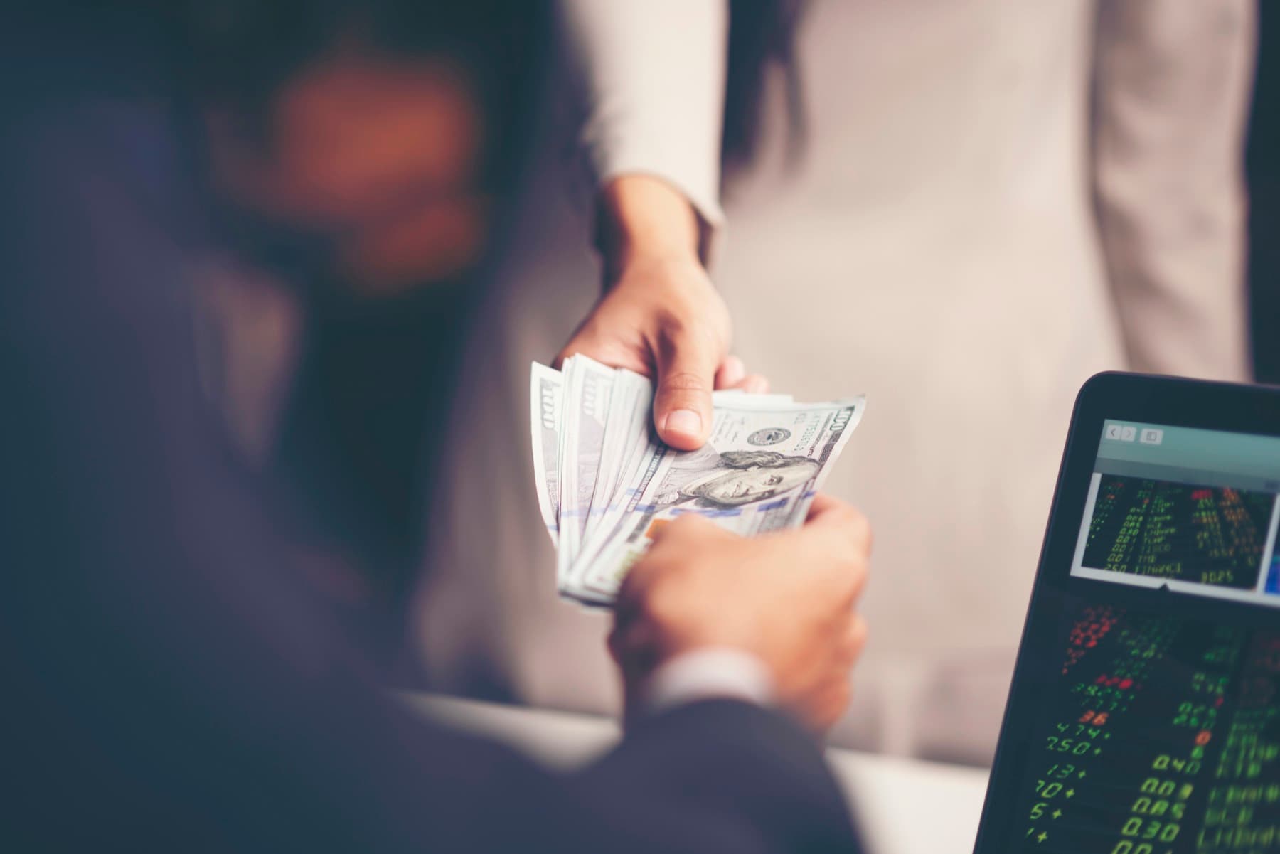 US dollar banknotes handed over beside a screen showing exchange rates